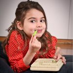 Child cheekily holds a game piece from the Smart Games Temple Trap Puzzle